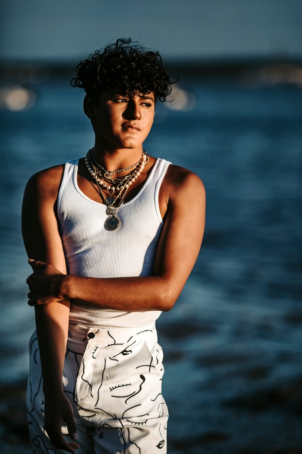 high school Senior boy in sleeveless fringe and many collars, at the beach in Massachusetts.