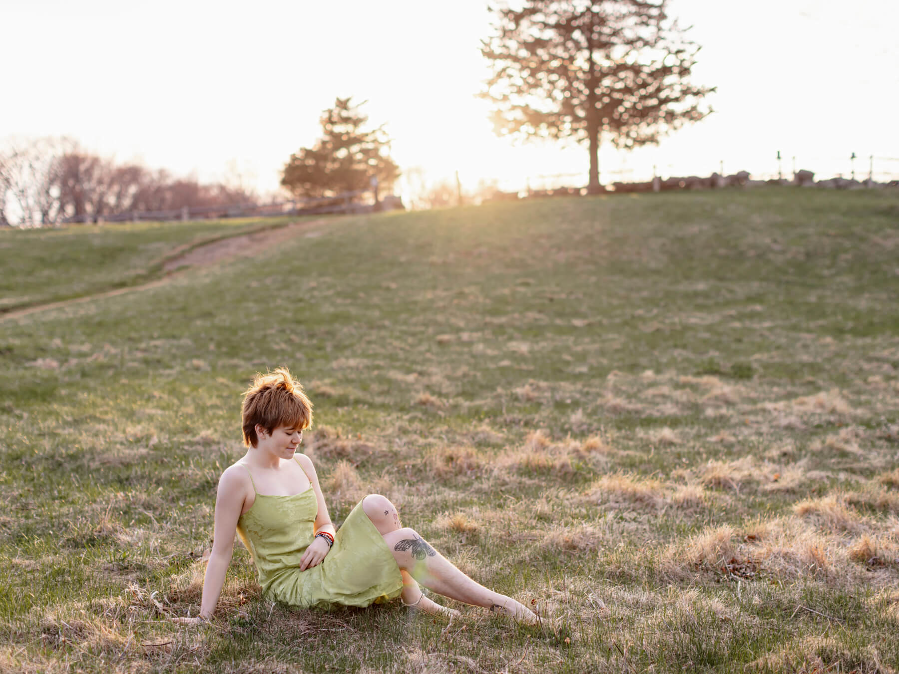 high school Senior boy in a green dress laying on the open filed, at Lexington, MA