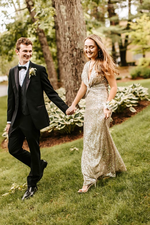 High school senior girl in a gold dress walking with her boyfriend, with a green and white trees as background, at Lexington, Massachusetts