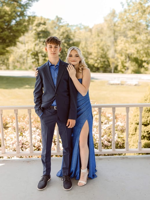 High school senior girl in a blue dress holding her boyfriend, with trees as background, at Lexington, Massachusetts