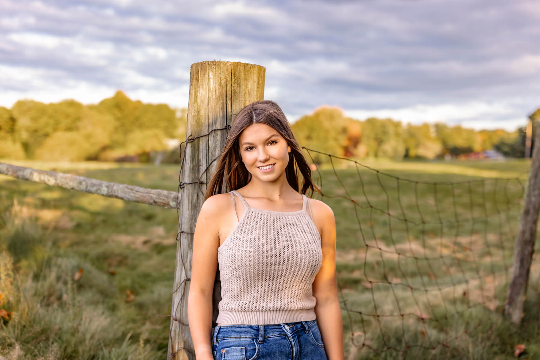 High School senior girl leaning on a fence with a field behind, at Lexington, MA