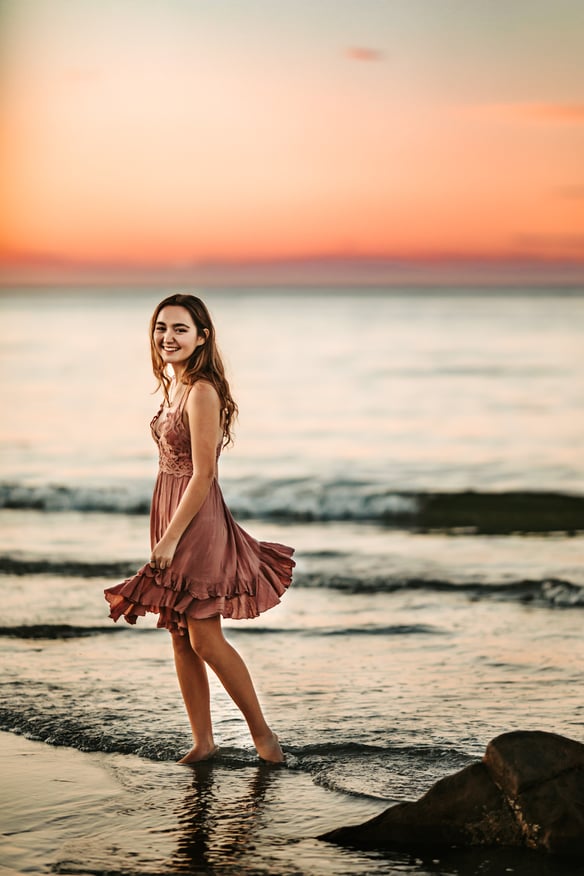 high school Senior girl with rose dress walking on the beach shore in Massachusetts