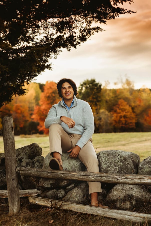 high school Senior boy sitting on the rocks with peak fall foliage, at Lexington, MA