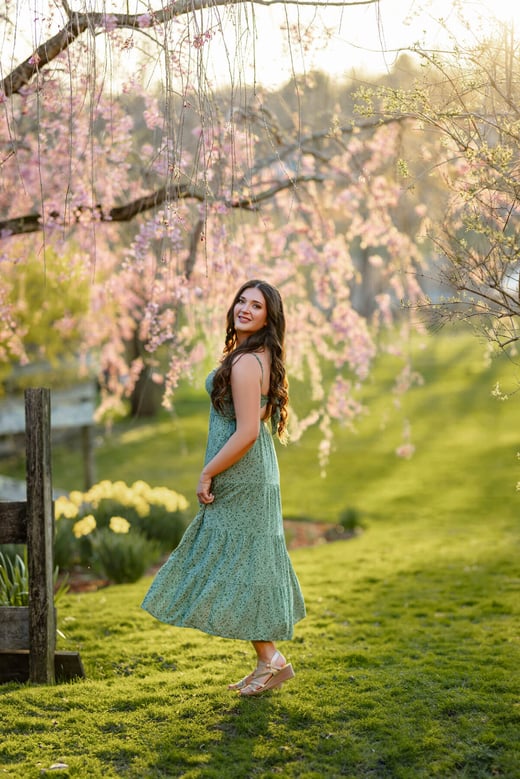 high school Senior girl in a green dress moving and posing in front of a pink flower tree, at Lexington, MA 