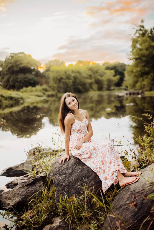 high school Senior girl with a flower dress sitting on the rocks near the lake, at Lexington, MA